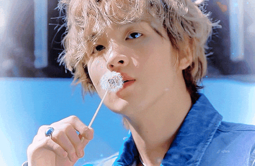 a young man blowing a dandelion with a blue background