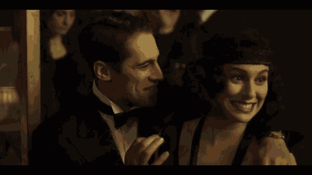 a man in a tuxedo and a woman in a flapper dress are smiling at each other