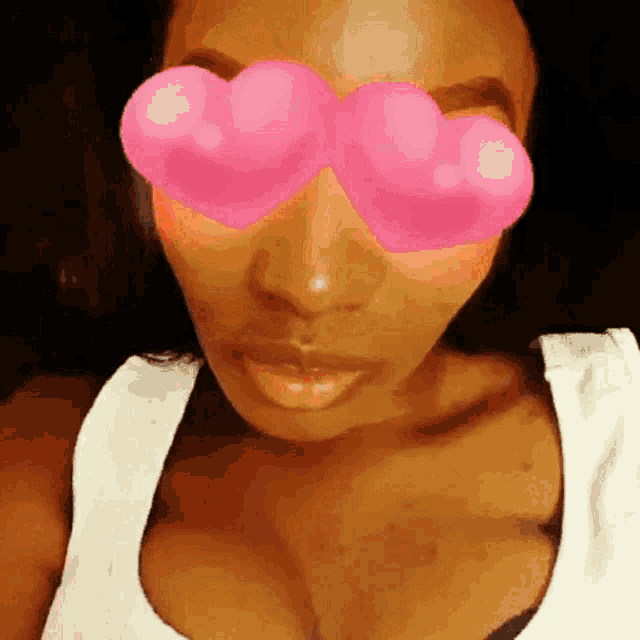 a woman wearing a white tank top has pink heart shaped sunglasses on her eyes