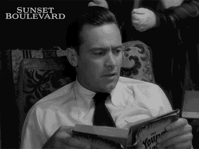 a man sitting in a chair reading a book with sunset boulevard written above him