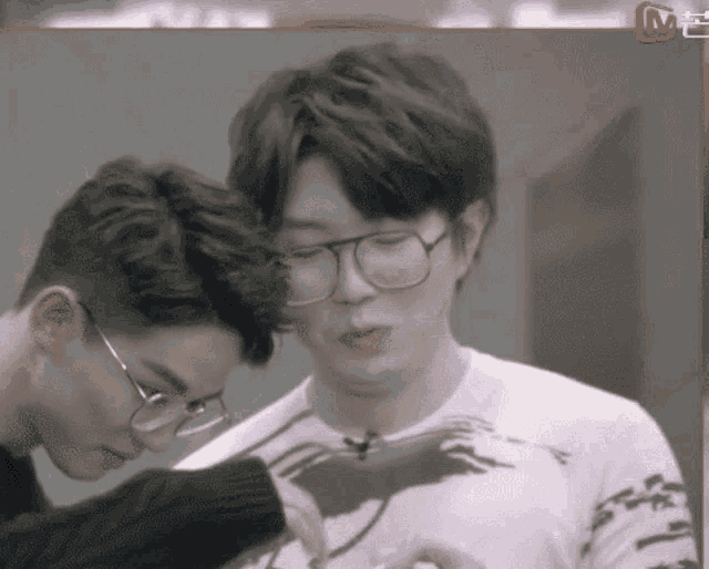 two men wearing glasses and a shirt with a bird on it are looking at something
