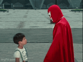 a man in a red cape is talking to a little boy in a white shirt