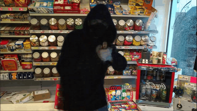 a man in a hooded costume stands in front of a coca cola fridge