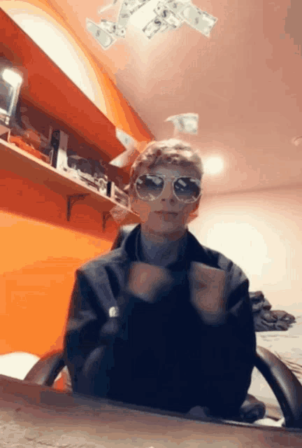 a man wearing sunglasses is sitting at a desk with money falling from the ceiling around him