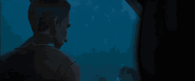 a man is looking out of a window at a fish tank
