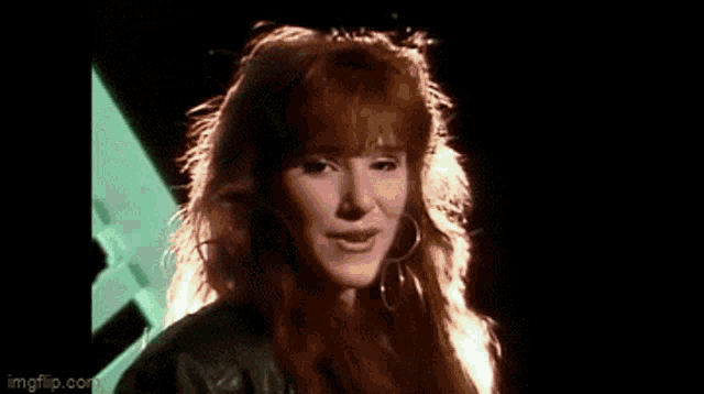 a woman with red hair is wearing hoop earrings and a black jacket