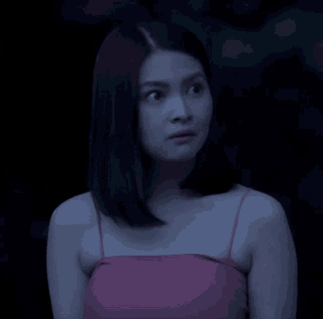 a woman in a pink tank top is making a face in the dark