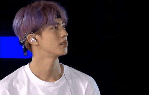 a young man with purple hair is wearing a white shirt and ear buds .