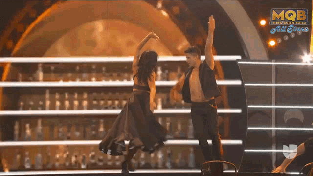 a man and a woman are dancing on a stage in front of a sign that says mqb