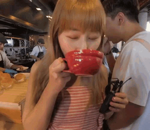 a woman is drinking from a red cup in a restaurant kitchen