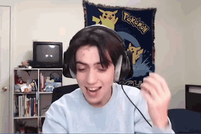 a young man wearing headphones is sitting in front of a pokemon wall hanging .