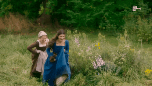 a woman in a blue dress is walking in a field with two other women .