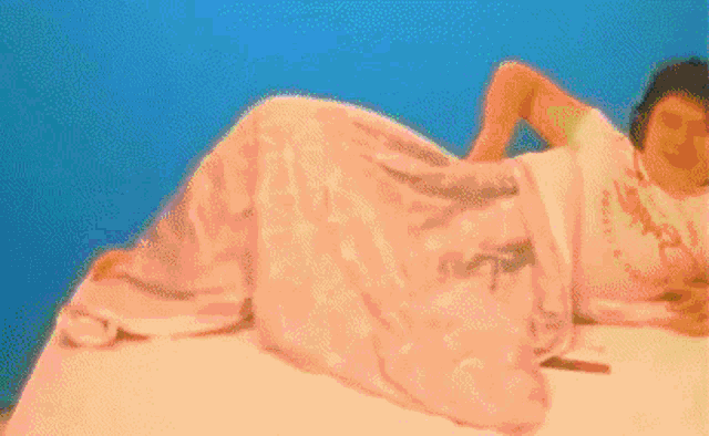 a woman is laying on a bed with a pink blanket on her .