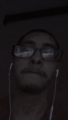a man wearing glasses and ear buds makes a funny face