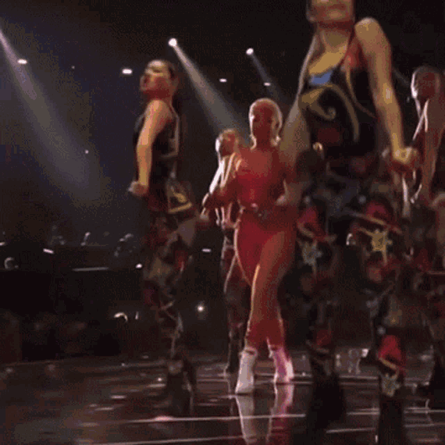 a woman in a pink bodysuit is dancing on a stage with other women