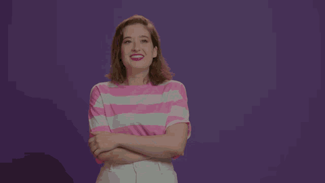 a woman wearing a pink and white striped shirt is standing with her arms crossed