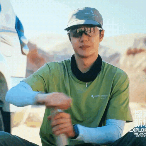 a man wearing sunglasses and a hat is sitting in the desert