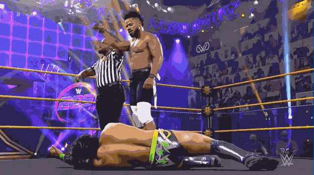 a wrestler is laying on the ground while a referee stands behind him