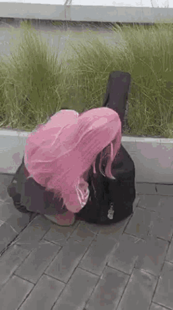 a woman with pink hair is kneeling down next to a guitar case on the sidewalk .