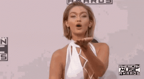 a woman in a white dress is blowing a kiss while standing on a red carpet at the american music awards .