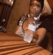 a woman is sitting at a table with a bottle of water in front of her face .