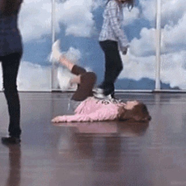 a girl is laying on the floor in a dance studio while another girl stands behind her .