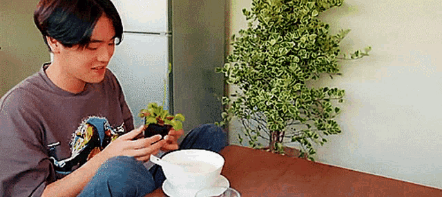 a young man is sitting at a table with a cup of coffee and a plant .