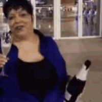 a woman in a blue jacket is sitting on the ground holding a bottle of beer .