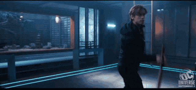 a man is holding a sword in a dark room with a dc universe logo on the bottom