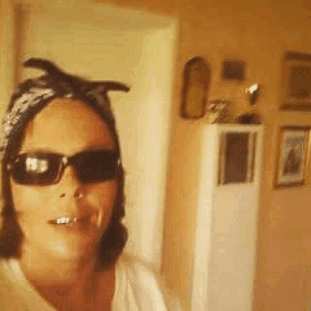 a woman wearing sunglasses and a bandana is taking a picture of herself in a room .