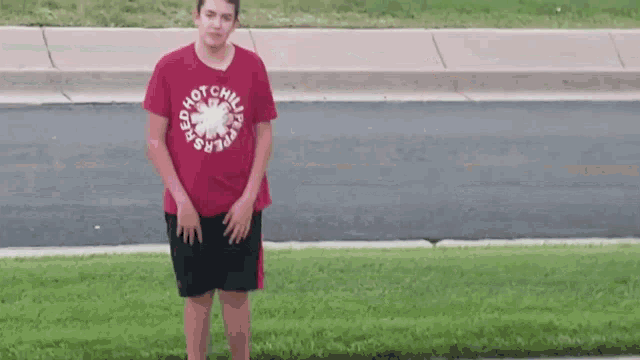 a young man wearing a red hot chili peppers t-shirt is standing in the grass .