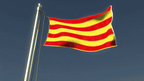 a red and yellow flag is flying in the wind against a blue sky