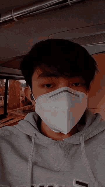 a young man wearing a gray hoodie and a white mask