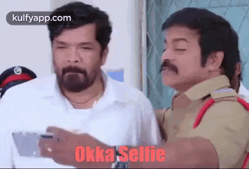 two men are standing next to each other and one of them is taking a selfie with a cell phone .