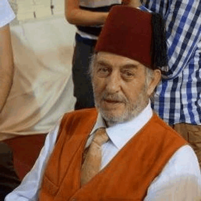 a man with a beard is wearing a fez hat and a vest and tie .