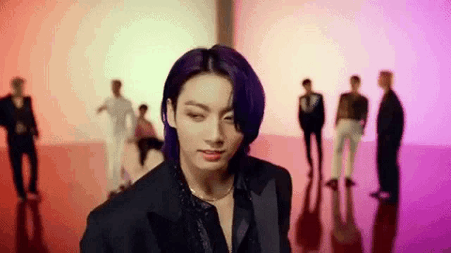 a man with purple hair is standing in front of a group of people in a room .