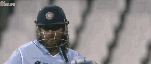 a cricket player wearing a helmet and sunglasses is standing in front of a fence .
