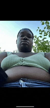 a man wearing a green top and blue shorts looks down at his belly
