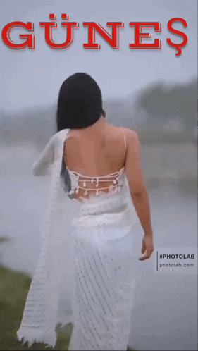 a woman in a white dress stands in front of a body of water with the word günes in red