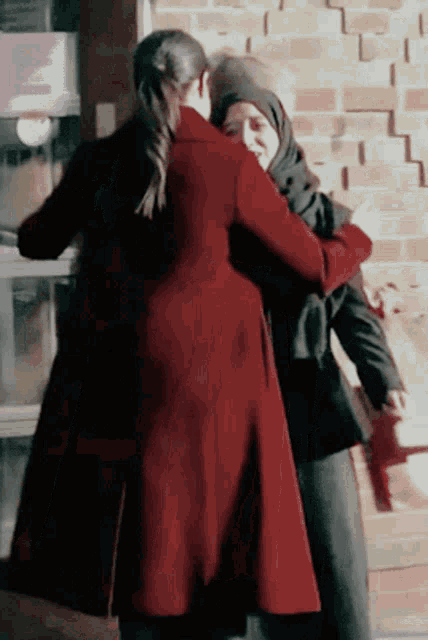 a woman in a red coat hugging another woman in a black hijab