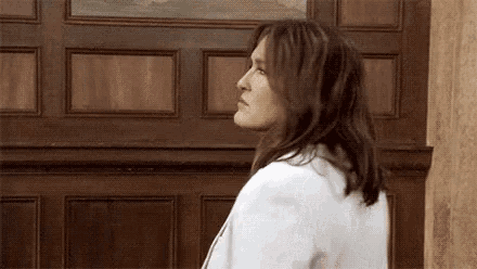 a woman in a white jacket is standing in front of a wooden door and looking up .