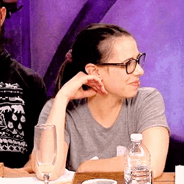 a woman wearing glasses sits at a table with a glass and a bottle of water