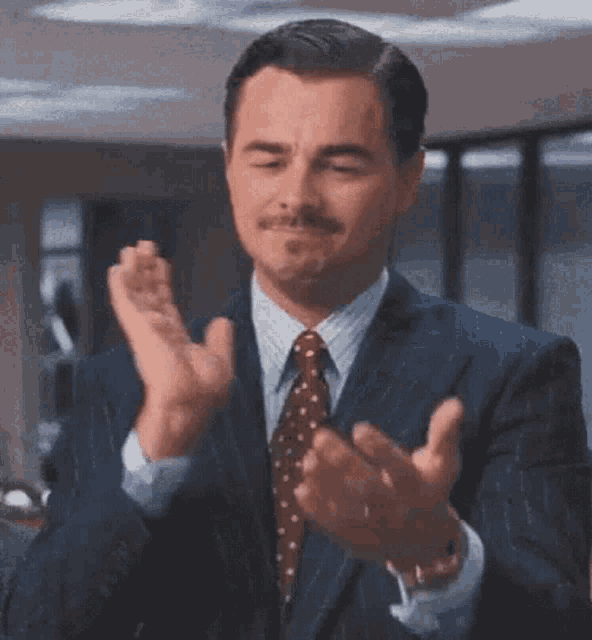 a man in a suit and tie is clapping his hands with his eyes closed .