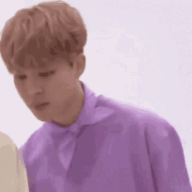 a young man wearing a purple shirt and tie is standing next to another young man .