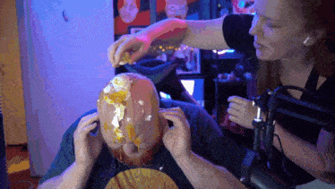 a man with a cake on his head is being decorated by a woman in front of a microphone