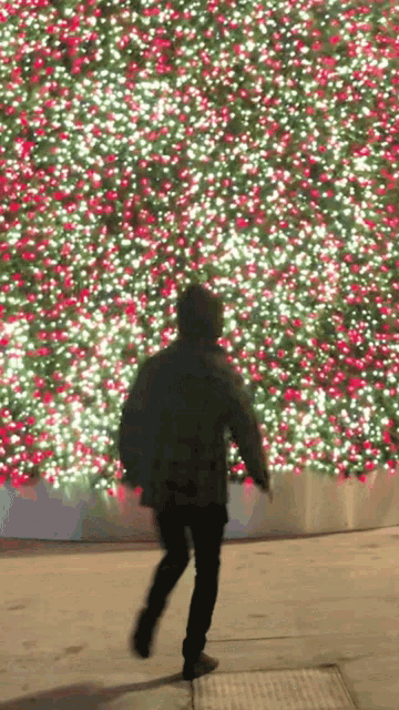 a person is walking in front of a christmas tree