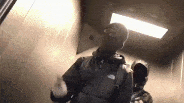 a man wearing a ski mask is walking down an elevator .