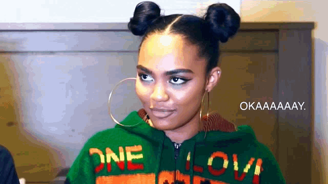 a woman wearing a green sweater that says one love on it