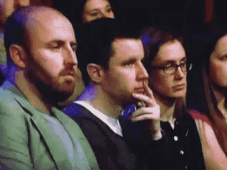 a group of people are sitting in a theatre watching a show and one man is holding his hand to his mouth .