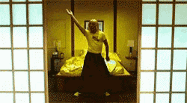 a man in a yellow shirt is dancing in front of a yellow bed